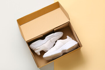 Cardboard box with sports shoes on color background