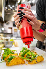 Close-up of hands garnishing a dish with sauce from a squeeze bottle, highlighting culinary artistry and precision. Perfect for food blogs, culinary magazines, and cooking tutorials.