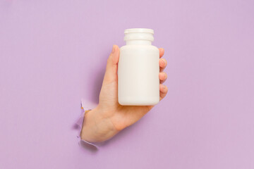 View on white bottle plastic tube in hands on lilac background. Packaging for pills, capsules, supplements. Cosmetics