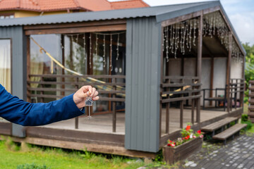 Keys in hand with new house at background. Broker, mortgage, property, real estate concept. Buying or renting