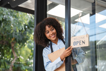Smiling Female Barista Opening Coffee Shop Door with Welcome Sign on a Bright Day