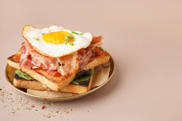 Delicious sandwich with fried egg and bacon on beige background