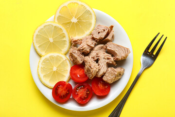 Plate with delicious canned tuna, fresh lemon, tomatoes and fork on yellow background