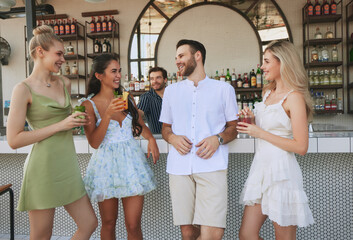 Happy young people, men and women, friends enjoy relaxing time in bar, drinking cocktail, having fun and good time. Summer vibe. Concept of friendship, party, leisure, celebration, relaxation
