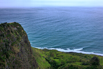 Narrow promontory rising high above over calm blue waters of Tasman Sea. Te Toto Gorge Lookout, Raglan, New Zealand