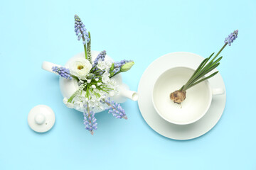 Composition with beautiful Muscari flowers in teapot and cup on blue background