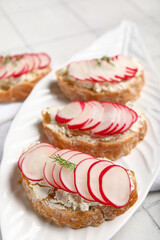 Plate with delicious radish bruschettas on white tiled table