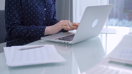 A female accountant or businesswoman with blue dotted blousy is typing on laptop computer on glass...