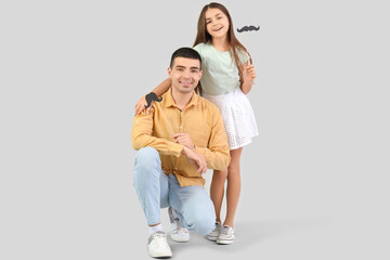 Fototapeta premium Portrait of father and his little daughter with paper mustache on light background