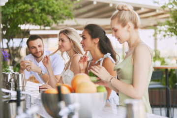 Friends, man and beautiful young women enjoying cocktails and friendly atmosphere at chic outdoor bar. Weekend vibes and refreshment. Concept of friendship, party, leisure, celebration, relaxation