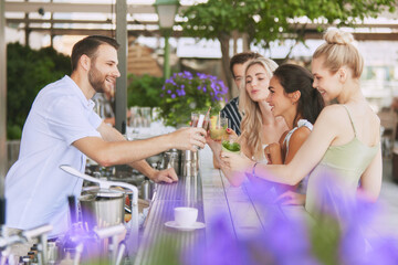 Group of friends, men and women enjoys refreshing cocktails in relaxed outdoor setting, modern bar, drinking with bartender. Concept of friendship, party, leisure, celebration, relaxation