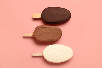 Different chocolate covered ice cream on stick against pink background
