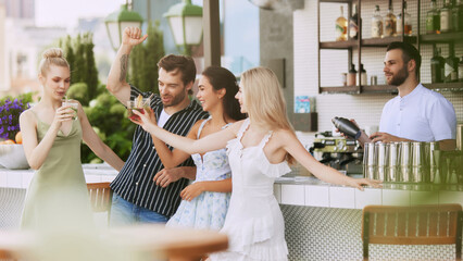 Group of happy young people, men and women meeting in modern outdoor bar, restaurant, drinking cocktails, enjoying company and conversation. Friendship, party, leisure, celebration, relaxation concept