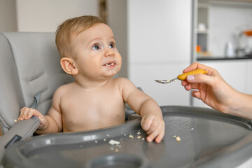 Nine month baby boy eating in dining chair, learning eating with spoon, feeding concept