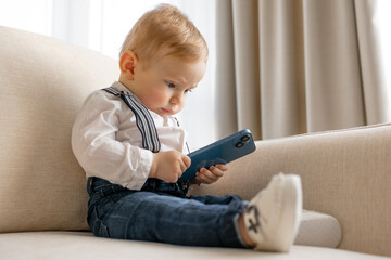 Cute Baby Using Smartphone While Sitting On Sofa At Home