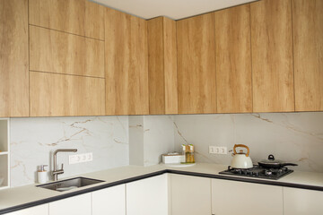 Modern kitchen interior with wooden cabinets, marble backsplash, and stainless steel appliances in a bright home