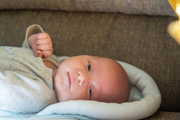 Portrait of Adorable Caucasian newborn baby lying down on sofa in living room. Cute infant child boy living together with family at home. Baby health care, childcare and children development concept.