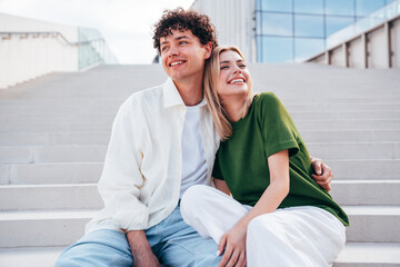 Smiling beautiful woman and her handsome boyfriend. Couple in casual summer clothes. Happy cheerful family. Female and man having fun. They posing in the street in sunny day. Sit at stairs