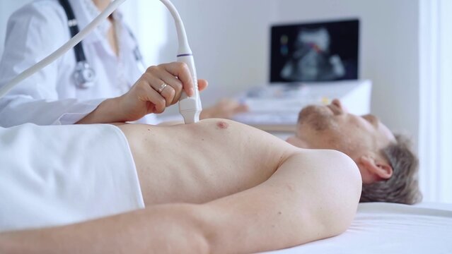 Doctor woman performing an ultrasound scan of male patient breast lying down in clinic procedure cabinet. Cardiology diagnosis and health care