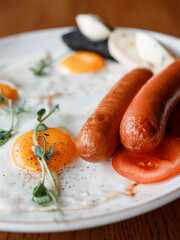 delicious English breakfast with juicy sausages, fresh vegetables, fragrant herbs, and scrambled eggs on a beautiful white plate in a cozy nice restaurant