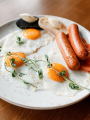 delicious English breakfast with juicy sausages, fresh vegetables, fragrant herbs, and scrambled eggs on a beautiful white plate in a cozy nice restaurant