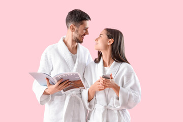 Happy young couple in robes with magazine and mobile phone on pink background