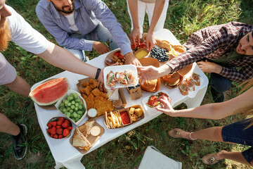 Close up view. Group of friends are having picnic on the field with food in eco boxes
