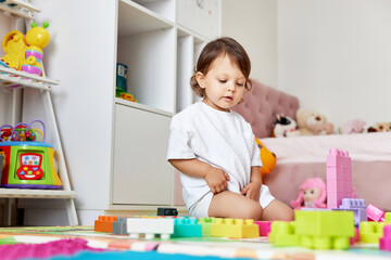 cute baby girl playing with colorful toys bricks at home