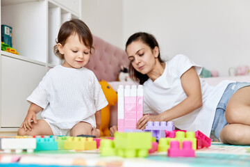 cute baby girl and her loving mother build tower from colorful cubes, early development