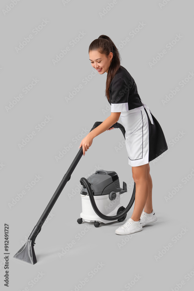 Sticker Young Asian chambermaid with vacuum cleaner on light background