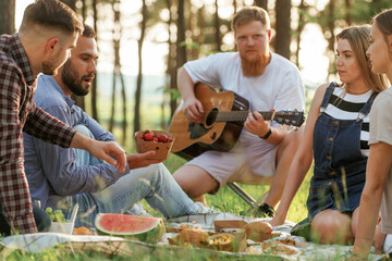 Summertime bonding. Group of friends are having picnic on the field with food in eco boxes
