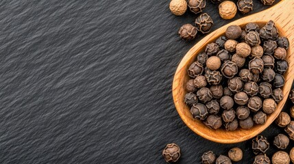 Black pepper on a wooden spoon over a black background with copy space, in a top view. 