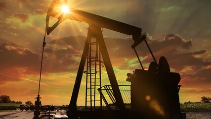 Silhouette of oil pump jack against a colourful beautiful sky with glowing clouds at sunset
