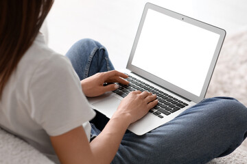 Naklejka premium Young woman sitting on sofa and using laptop in living room, closeup