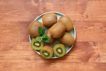 Plate with fresh kiwi and mint on wooden background