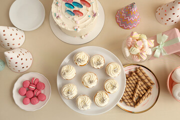 Dessert stand with tasty white cupcakes and other sweets for birthday party on beige table
