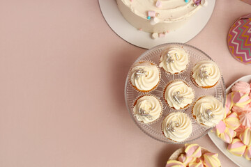 Dessert stand with tasty white cupcakes and other sweets for birthday party on pink table