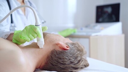 Doctor woman with green medical gloves performing neck ultrasound exam on male patient. Thyroid...
