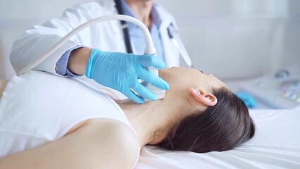 Obraz premium Doctor man wearing blue medical gloves is using ultrasound equipment on neck of female patient lying down for a medical examination