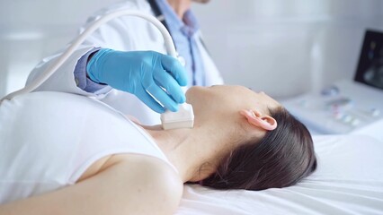 Naklejka premium Doctor man wearing blue medical gloves is using ultrasound equipment on neck of female patient lying down for a medical examination