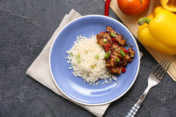 Tasty sweet and sour chicken with rice in plate, vegetables and fork on black grunge background