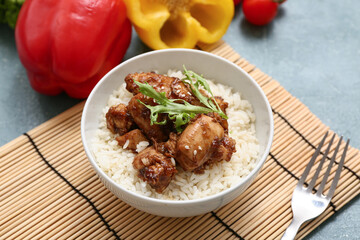 Tasty sweet and sour chicken with rice in bowl, mat and fork on turquoise grunge background, closeup