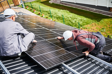Engineers installing photovoltaic solar panels on roof of house. Men technicians in helmets...
