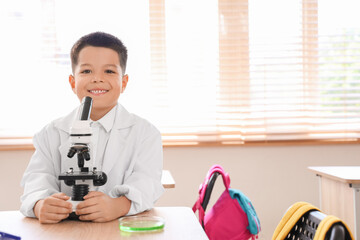 Cute little boy with microscope in science classroom