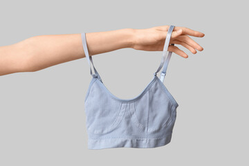 Female hand with stylish cotton bra on grey background, closeup