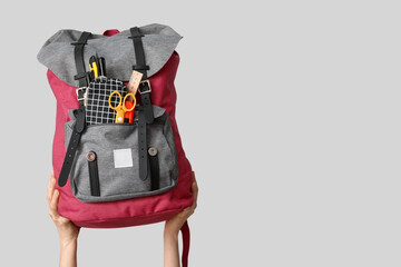Female hands with backpack and different school supplies on grey background, closeup