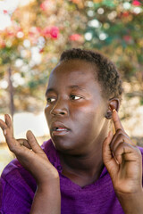 portrait of village African woman, with hands gesture, short hair, sited outdoors in the garden