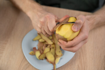 Male Hands peeling potato with kitchen knife, top view. Food preparation