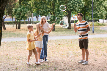 Fototapeta premium Happy family with cute children blowing soap bubbles in park