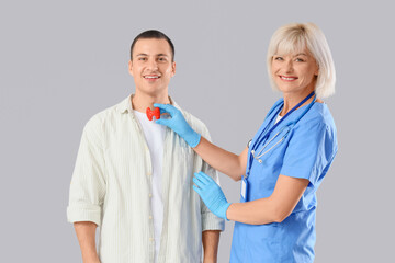 Female endocrinologist with thyroid gland model and man on light background